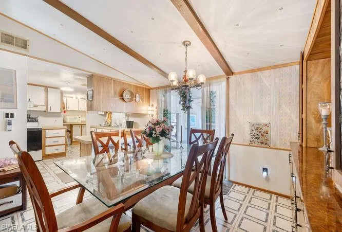 Dining space with vaulted ceiling with beams, wooden walls, and an inviting chandelier