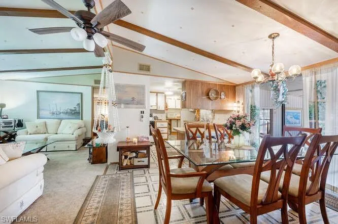 Carpeted dining area with vaulted ceiling with beams, wood walls, and ceiling fan with notable chandelier