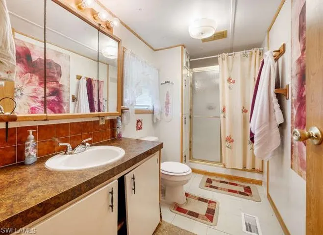 Bathroom featuring vanity, backsplash, tile patterned floors, and a shower with door