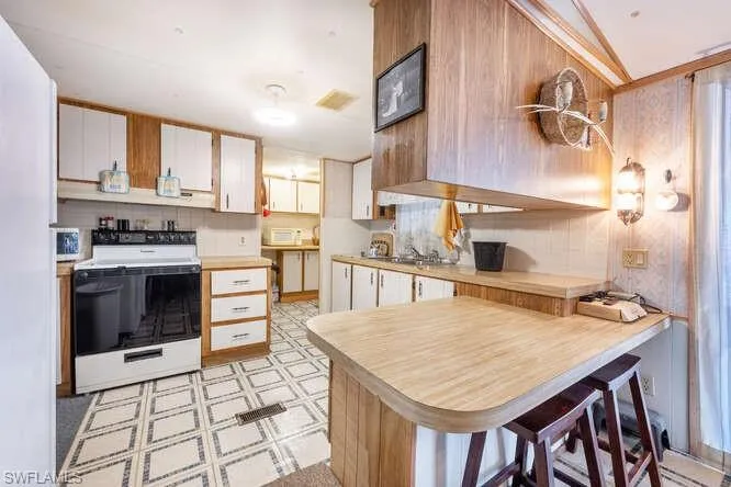 Kitchen featuring sink, a kitchen breakfast bar, kitchen peninsula, white appliances, and white cabinets