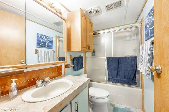 Full bathroom featuring vanity, toilet, combined bath / shower with glass door, and tasteful backsplash