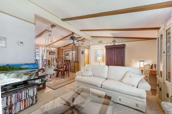 Living room featuring lofted ceiling with beams, light colored carpet, and ceiling fan