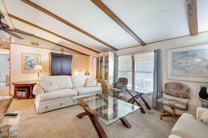 Living room with vaulted ceiling with beams, ceiling fan, and carpet floors