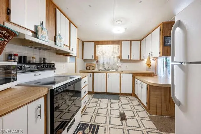 Kitchen featuring tasteful backsplash, white cabinetry, sink, and white appliances