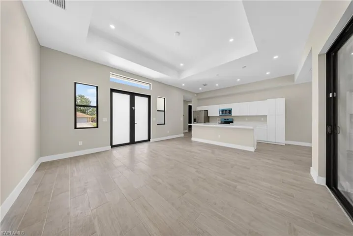 Open-concept living space featuring wood-finish flooring, a tray ceiling with recessed lighting, and a kitchen with white cabinetry and an island