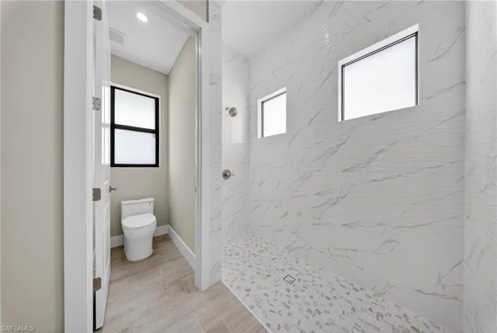 Spacious walk-in shower featuring large format wall tiling with subtle wave texture and two transom windows