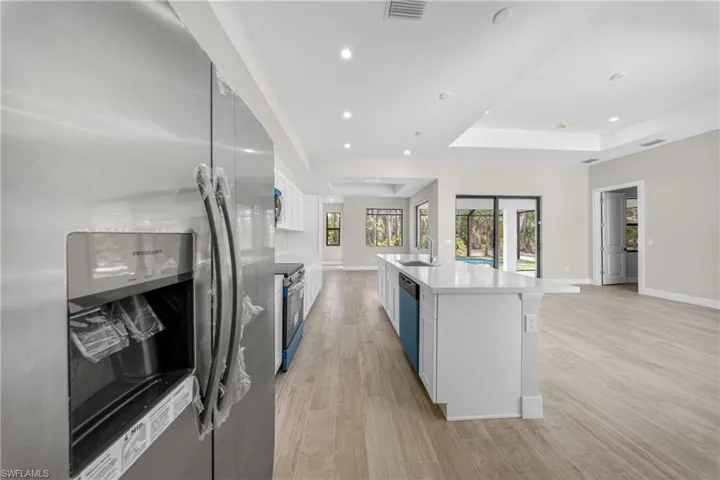 Kitchen featuring a white island with an integrated sink, stainless steel appliances, and light wood-finish flooring