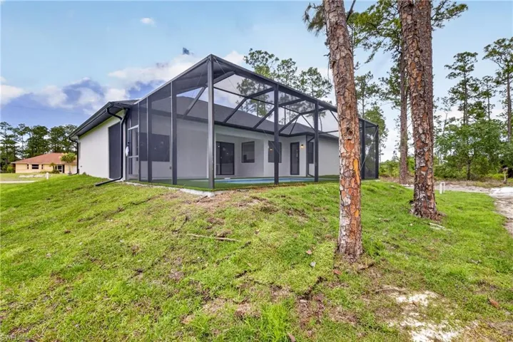 Rear exterior featuring a screened-in lanai, clear pool, and ample green space