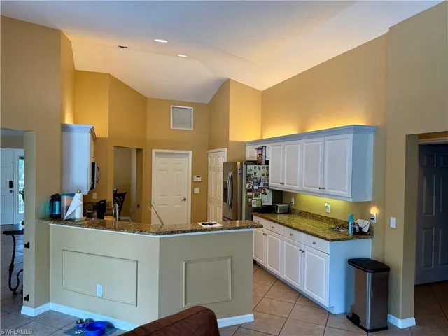 Kitchen featuring high vaulted ceiling, stainless steel fridge with ice dispenser, light tile patterned flooring, white cabinets, and dark stone countertops