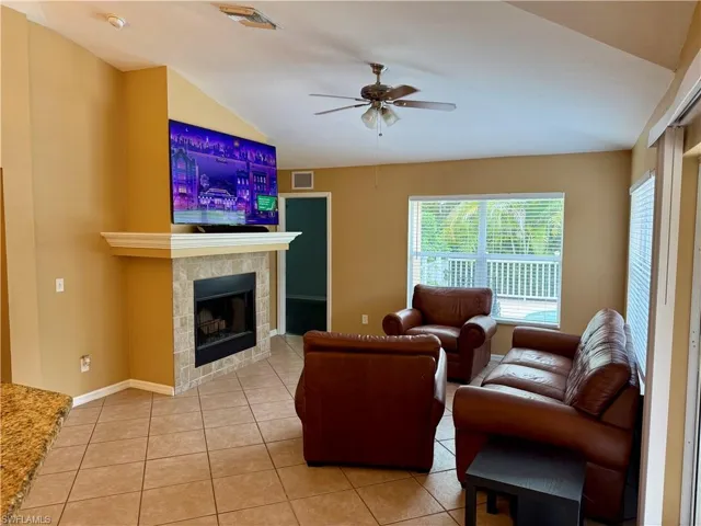 Living room with ceiling fan, light tile patterned flooring, a fireplace, and vaulted ceiling