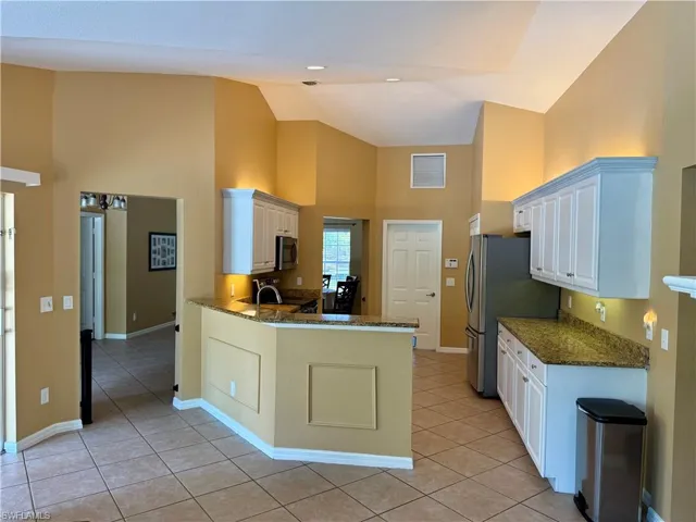 Kitchen with high vaulted ceiling, stainless steel appliances, light tile patterned flooring, and white cabinets