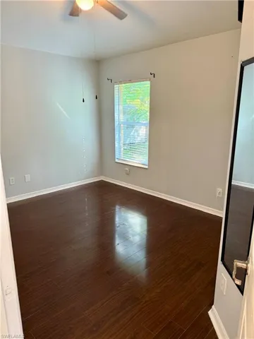 Empty room featuring a ceiling fan and dark wood-style floors