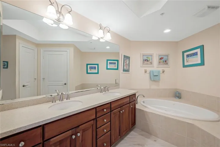 Bathroom with a relaxing tiled bath, oversized vanity, double sink, a notable chandelier, and tile floors