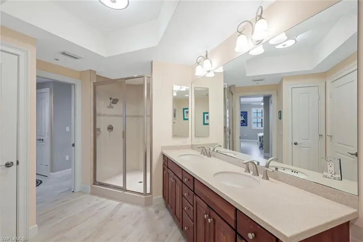 Bathroom featuring a raised ceiling, an enclosed shower, double vanity, and hardwood / wood-style flooring