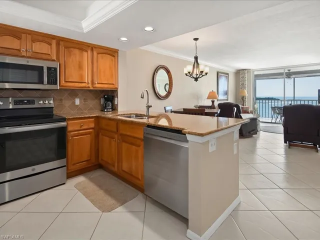 Kitchen with crown molding, appliances with stainless steel finishes, brown cabinetry, light stone counters, and open floor plan