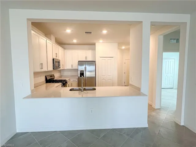 Kitchen with stainless steel appliances, white cabinetry, light stone countertops, recessed lighting, and a peninsula