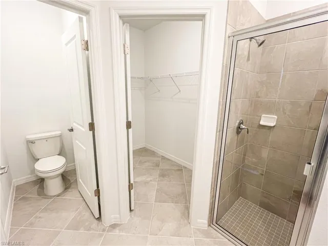 Full bathroom featuring a stall shower, a spacious closet, and light tile patterned floors