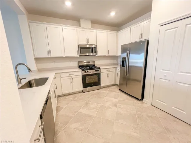 Kitchen with stainless steel appliances, white cabinets, and light stone countertops