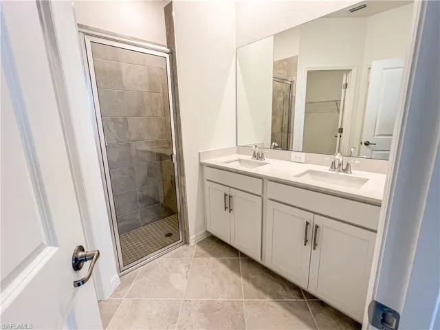 Full bathroom featuring double vanity, a shower stall, and a walk in closet