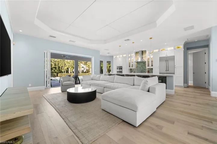 Light-filled living with warm flooring, custom lighting, and effortless indoor–outdoor access through French doors.