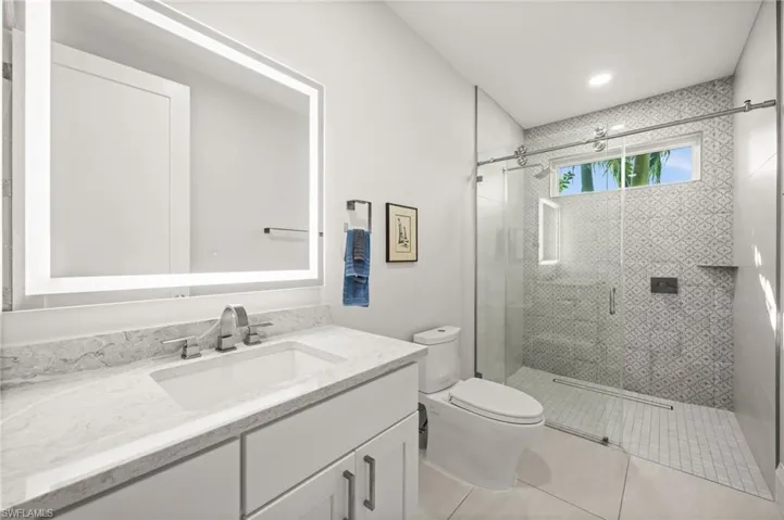 A modern guest bath with quartz countertops, backlit mirror, and a glass-enclosed walk-in shower.