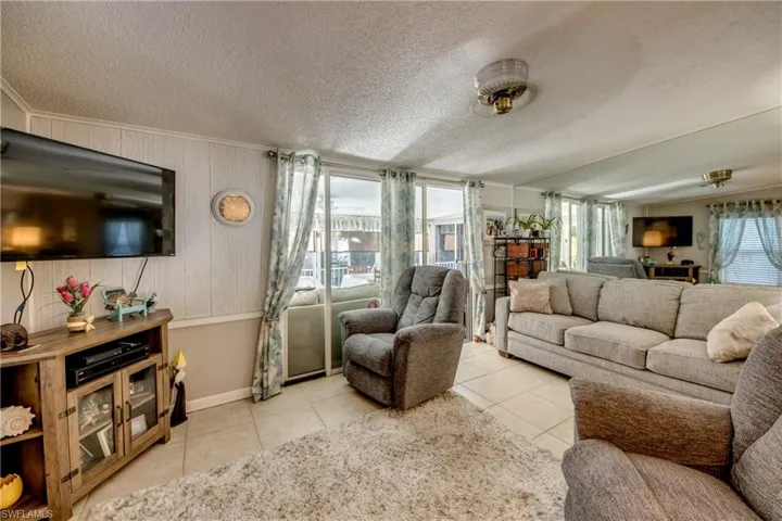 Living room featuring wooden walls, ornamental molding, a textured ceiling, and light tile patterned floors