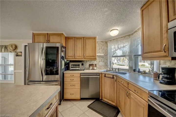 Kitchen featuring appliances with stainless steel finishes, a textured ceiling, light countertops, light tile patterned floors, and decorative backsplash