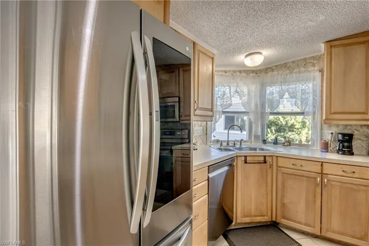 Kitchen featuring appliances with stainless steel finishes, light countertops, light brown cabinetry, a textured ceiling, and backsplash