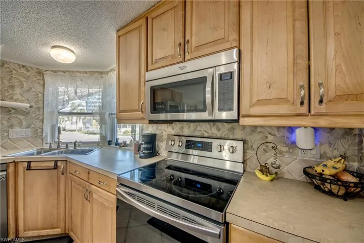 Kitchen featuring appliances with stainless steel finishes, light countertops, tasteful backsplash, a textured ceiling, and light brown cabinetry