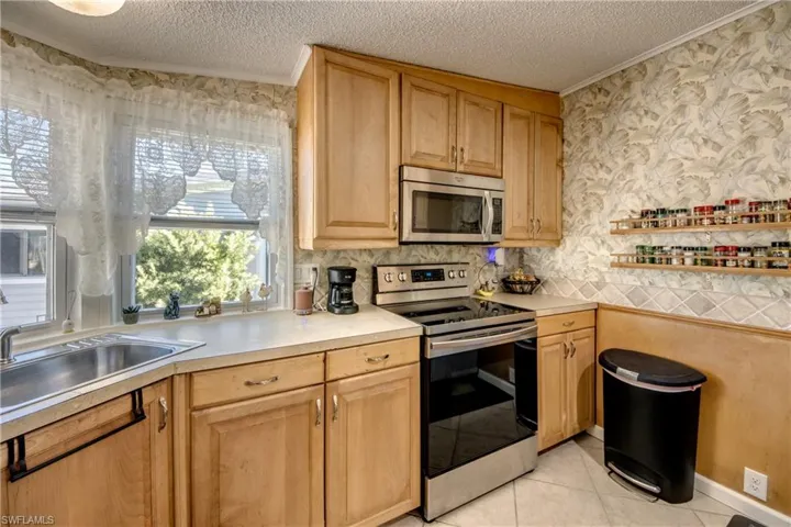 Kitchen featuring appliances with stainless steel finishes, light countertops, light tile patterned floors, backsplash, and a textured ceiling
