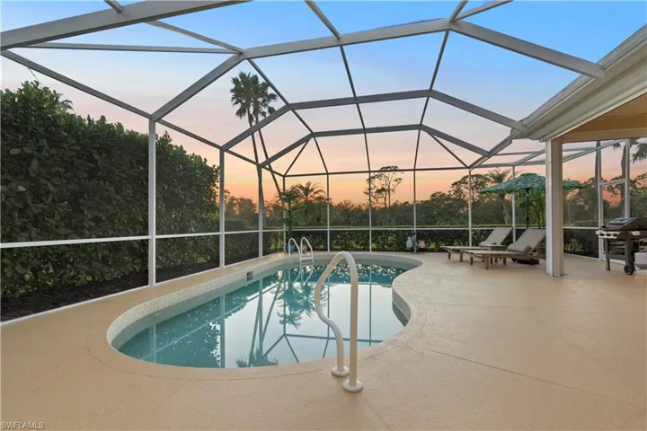 Pool at dusk with glass enclosure, area for grilling, and a patio area