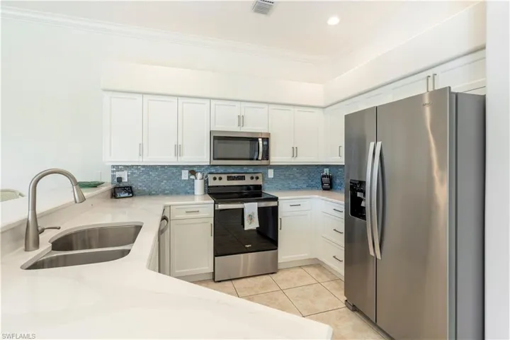 Kitchen with decorative backsplash, appliances with stainless steel finishes, crown molding, sink, and white cabinetry