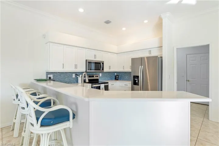 Kitchen with backsplash, white cabinets, a kitchen breakfast bar, kitchen peninsula, and stainless steel appliances