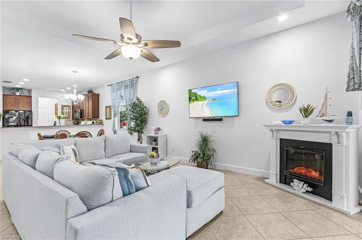 Living area featuring a ceiling fan, a glass covered fireplace, light tile patterned flooring, and a chandelier