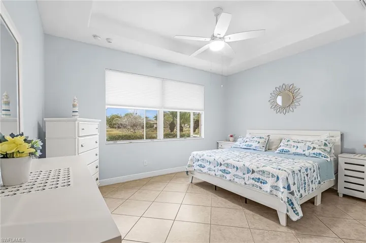 Primary bedrm with tray ceiling and sun-lit windows overlooking pool area.