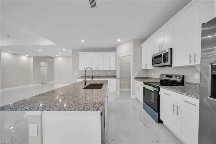 Kitchen featuring stainless steel appliances, light marble finish floors, white cabinets, a kitchen island with sink, and recessed lighting
