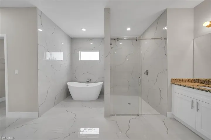 Bathroom featuring a marble finish shower, a freestanding bath, light marble finish floors, a walk in closet, and recessed lighting