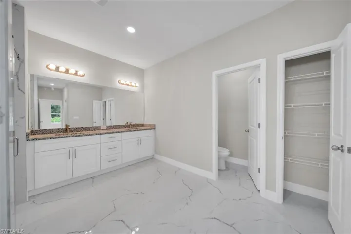 Bathroom with double vanity, light marble finish flooring, recessed lighting, and a marble finish shower