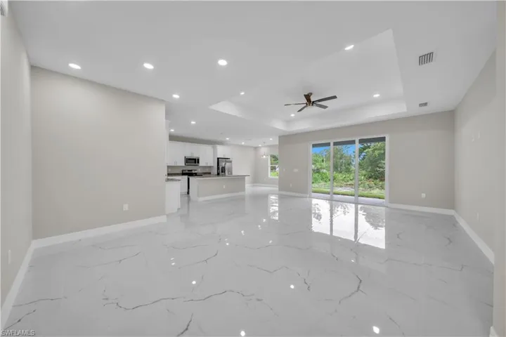 Unfurnished living room featuring a tray ceiling, recessed lighting, a ceiling fan, and light marble finish floors