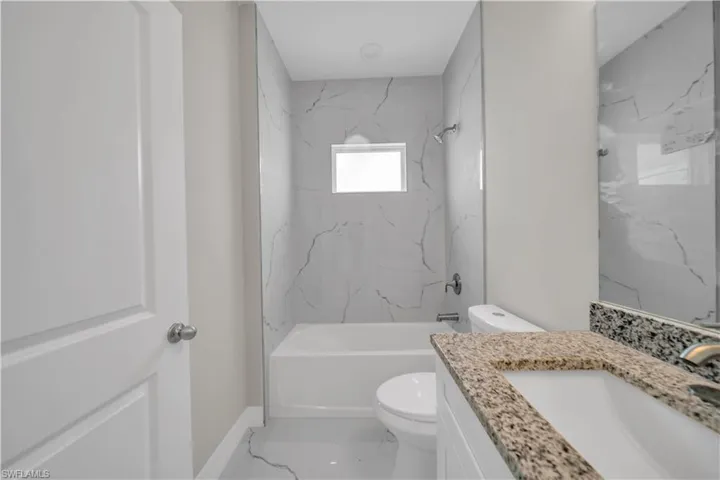 Full bath featuring vanity, a combined bath / shower with marble appearance, and marble look tiles
