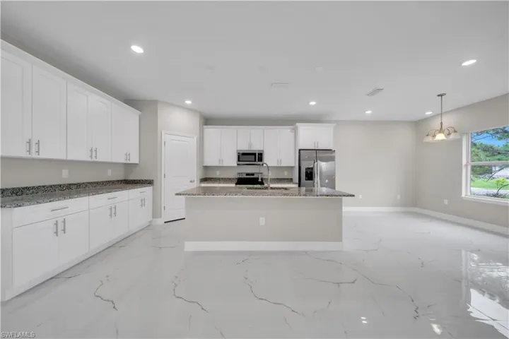Kitchen featuring white cabinets, appliances with stainless steel finishes, dark stone countertops, a kitchen island with sink, and light marble finish floors
