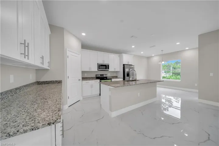 Kitchen featuring a kitchen island with sink, light stone countertops, white cabinets, recessed lighting, and light marble finish flooring