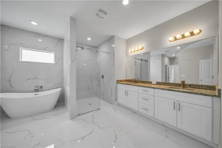Full bath with double vanity, a marble finish shower, a soaking tub, recessed lighting, and light marble finish flooring