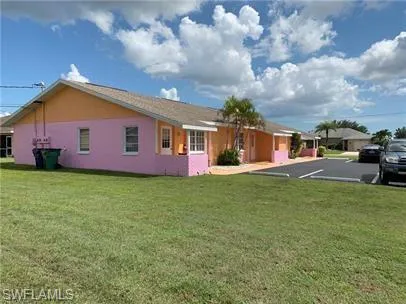 Rear view of property featuring a lawn, stucco siding, and uncovered parking