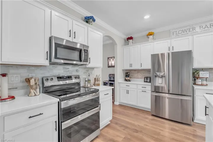 Kitchen with light hardwood / wood-style flooring, white cabinets, stainless steel appliances, and ornamental molding