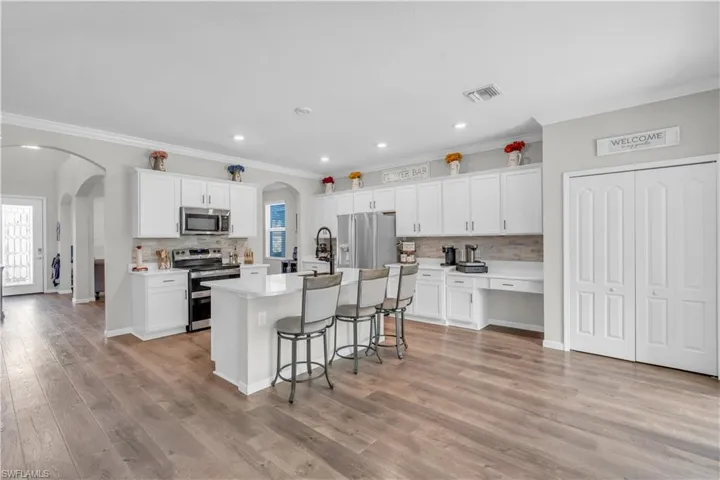 Kitchen with stainless steel appliances, white cabinetry, a kitchen island with sink, and light hardwood / wood-style flooring