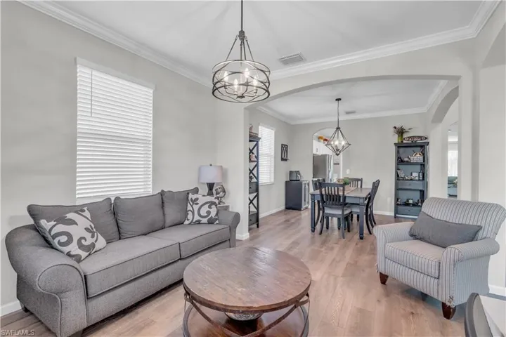 Living room with crown molding, wood-type flooring, and a notable chandelier