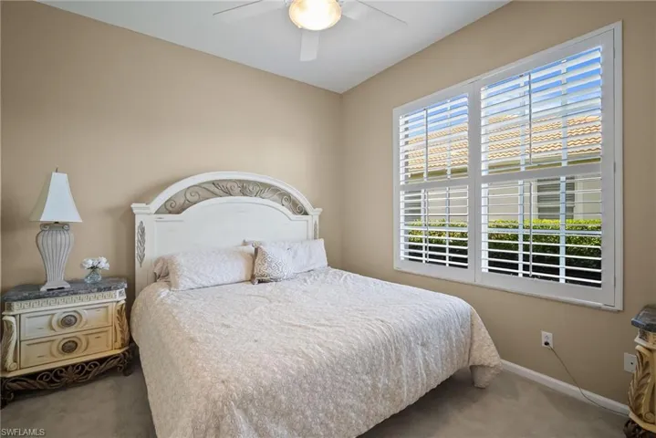 Carpeted bedroom with plantation shutters and ceiling fan.