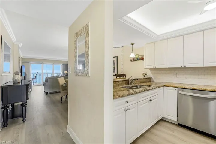 Kitchen featuring dark stone countertops, ornamental molding, light wood finished floors, dishwasher, and backsplash