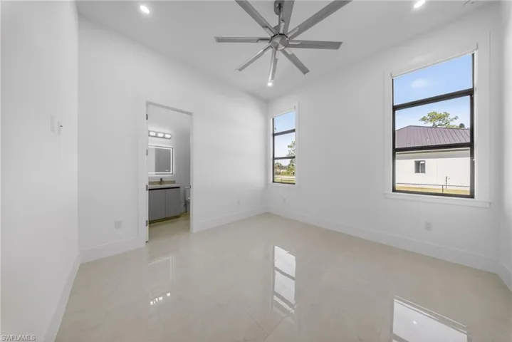 Bedroom featuring a walk-in closet, ensuite bathroom, oversize windows for natural light, curtains, and a ceiling fan.